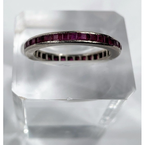 699 - A white metal eternity ring set rectangular cut rubies, unmarked, tests as 18 carat, size R-S
