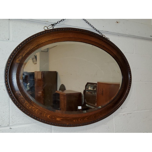 843 - A large canted rectangular beaded oak wall mirror; an oval wall mirror in an inlaid mahogany frame.