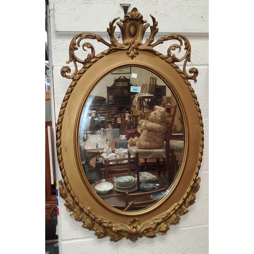 826 - An oval wall mirror in period style gilt frame with scrolled rococo crest, height 90 cm
