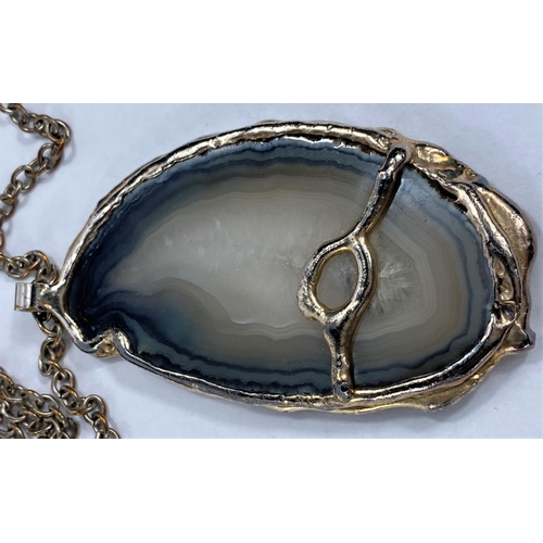 714 - A modernist rock specimen pendant in silvered metal surround, on chain