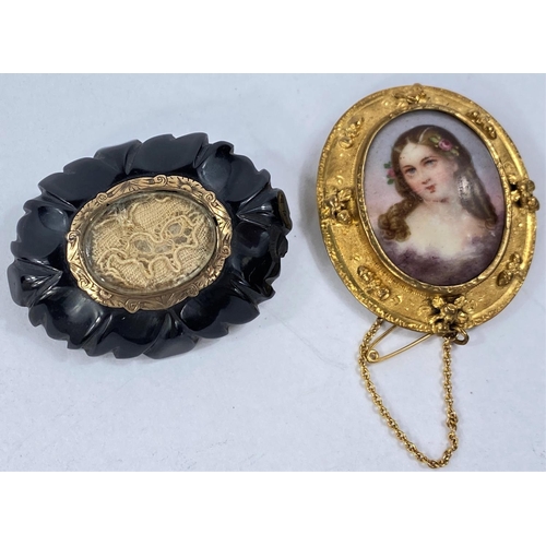 700A - A gilt framed cameo brooch with central porcelain oval, unmarked and an ebonised mourning brooch