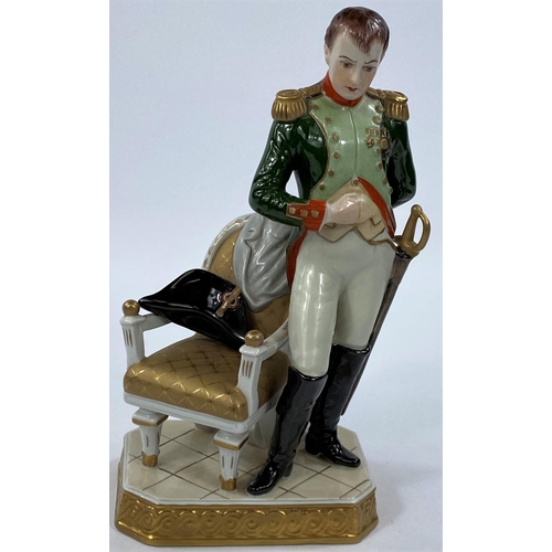 477 - NAPOLEON BONAPARTE,  a continental porcelain figure with Napoleon standing beside a chair, 23cm