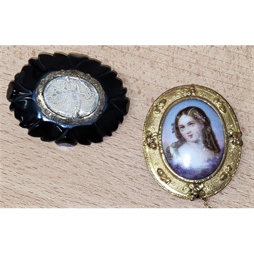 700A - A gilt framed cameo brooch with central porcelain oval, unmarked and an ebonised mourning brooch