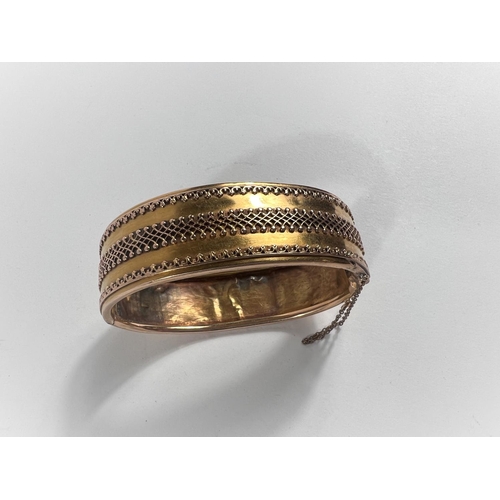 653 - A yellow metal bangle with fancy embossed central border and rims to one side, the other side plain ... 