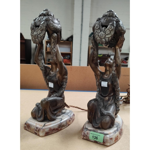 136 - An Art Deco pair of bronzed metal bedside lamps in the form of kneeling figures holding floral shade... 