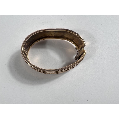 653 - A yellow metal bangle with fancy embossed central border and rims to one side, the other side plain ... 