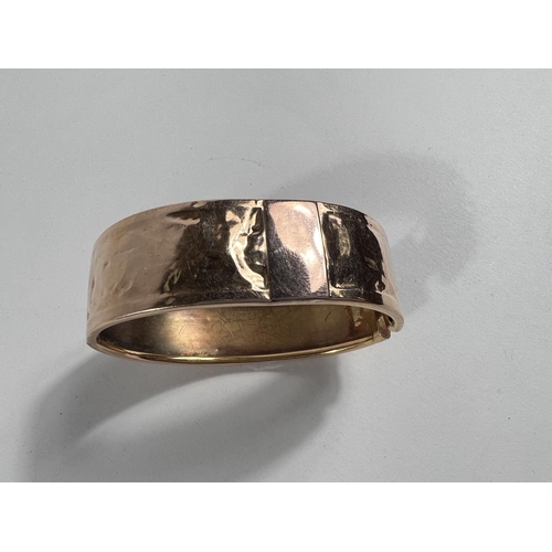 653 - A yellow metal bangle with fancy embossed central border and rims to one side, the other side plain ... 