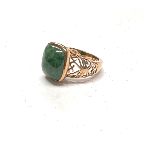 708 - A 9 carat hallmarked gold dress ring set with a square domed jade coloured stone with pierced scroll... 