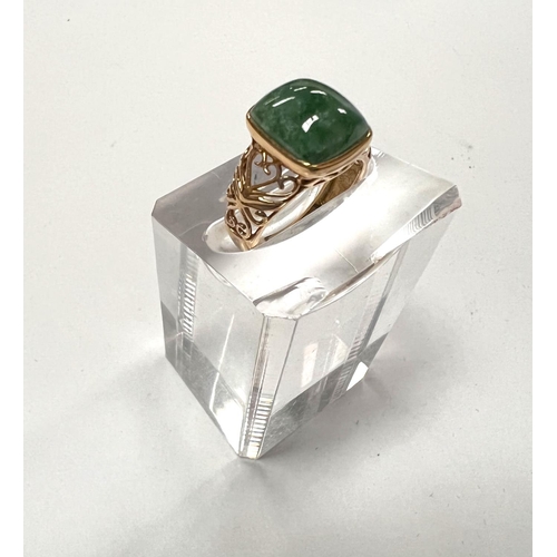 708 - A 9 carat hallmarked gold dress ring set with a square domed jade coloured stone with pierced scroll... 