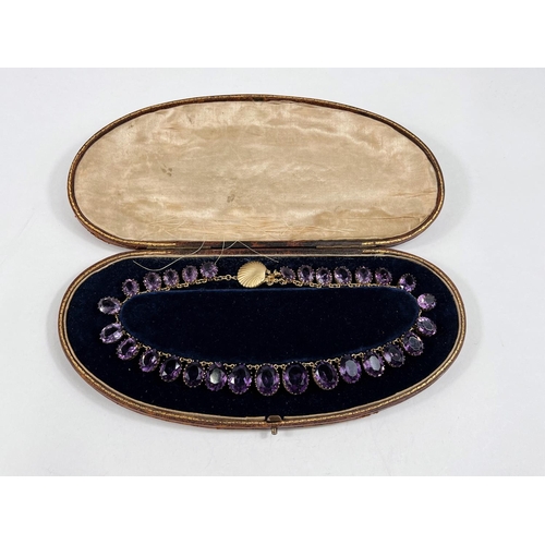 793 - A gilt metal rivière necklace set graduating amethyst coloured stones with shell clasp, stamped 'Nap... 