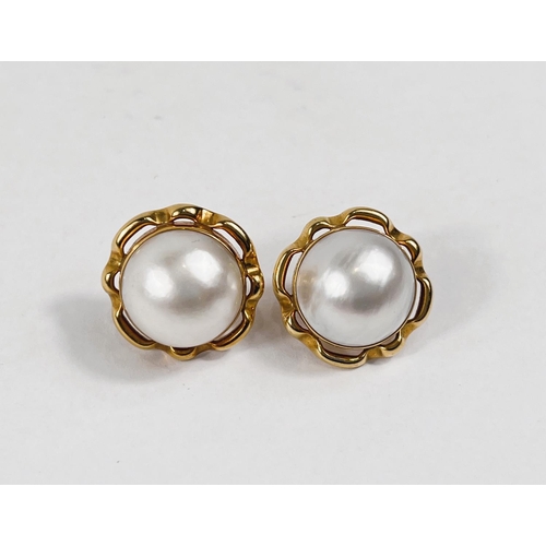 799 - A yellow metal pair of pierced earrings set with large mabe pearls in pierced surround with solid ba... 