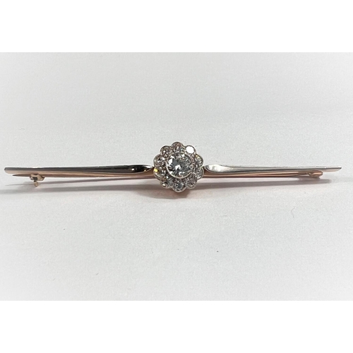 669 - A yellow metal bar brooch with 11 diamonds in flowerhead setting, central stone 5mm approx