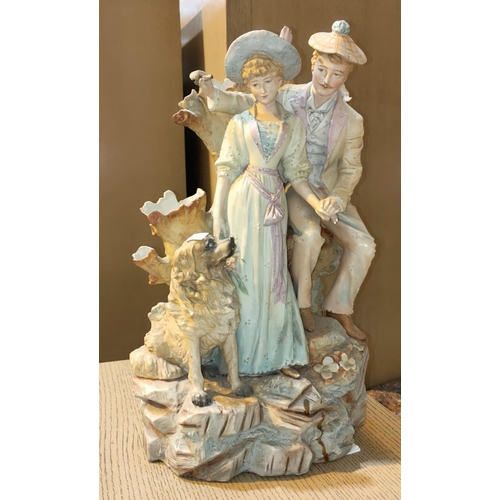 498 - A 19th century, coloured bisque courting couple with a dog, standing on rocks. height 43cm