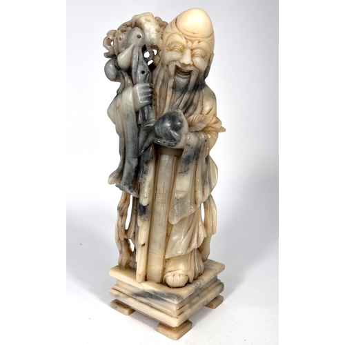 393 - A mottled grey and cream soapstone depicting an Immortal holding a peach and a staff height 25cm