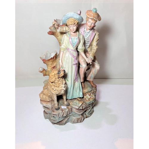 524 - A 19th century, coloured bisque courting couple with a dog, standing on rocks. height 43cm