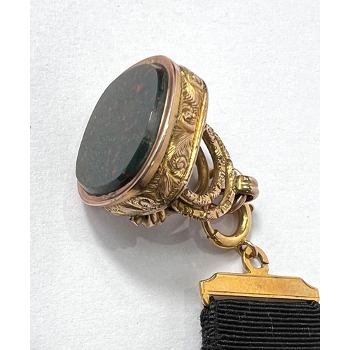 734 - A black silk ribbon with yellow metal clip and buckle; an ornate chased fob with green and red polis... 