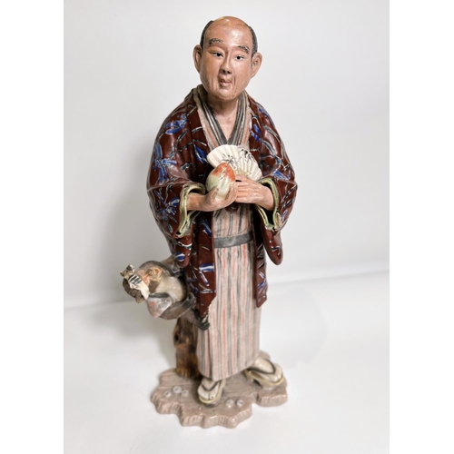 423 - A late 19th/ early 20th century ceramic figure of a man with fan and monkey hanging from his Haori i... 