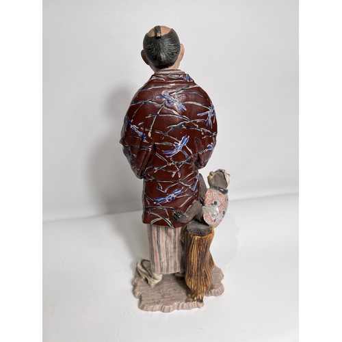 423 - A late 19th/ early 20th century ceramic figure of a man with fan and monkey hanging from his Haori i... 