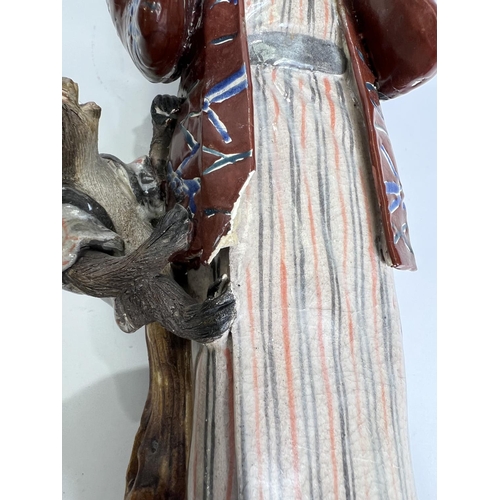 423 - A late 19th/ early 20th century ceramic figure of a man with fan and monkey hanging from his Haori i... 