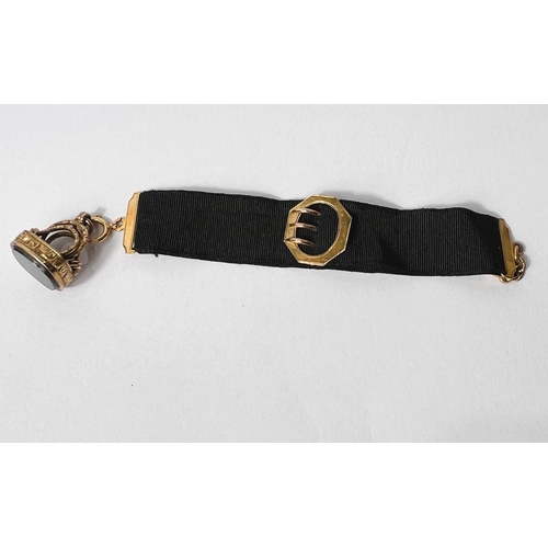 734 - A black silk ribbon with yellow metal clip and buckle; an ornate chased fob with green and red polis... 