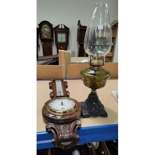 102 - An Edwardian barometer with thermometer in carved oak case; a cast iron and glass oil lamp