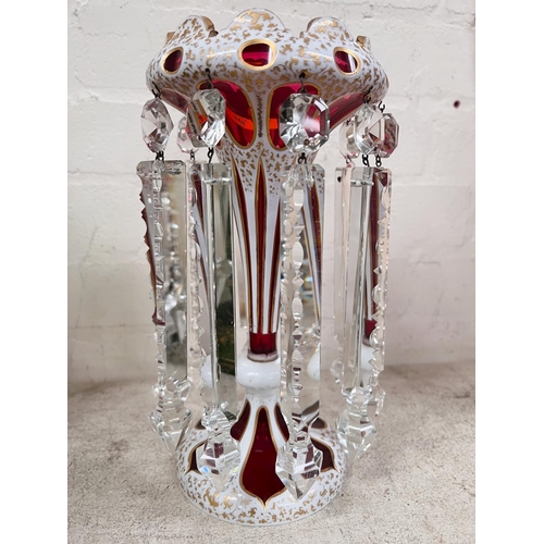 458 - A Victorian cranberry glass lustre, overlaid and cut back in opaque white with faceted drops, ht. 29... 