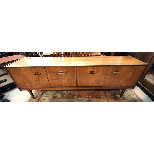 1046 - A mid 20th century designer teak long low sideboard with shaped protruding handles, three drawers an... 