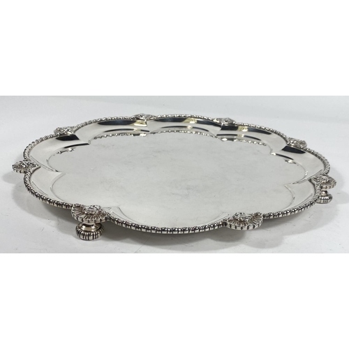 702 - A hallmarked silver scalloped circular tray with raised beaded border and sunburst facemask mounts, ... 