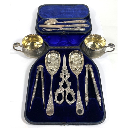 712 - An ornate set comprising berry spoons, nutcrackers and grape scissors, cased; a hallmarked silver ch... 