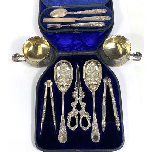 712 - An ornate set comprising berry spoons, nutcrackers and grape scissors, cased; a hallmarked silver ch... 