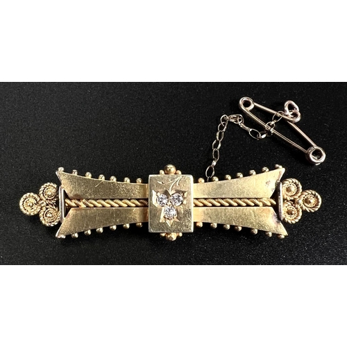 749 - A yellow metal bar brooch set with 3 diamonds and with filigree decoration, stamped 15ct, 4.7gm