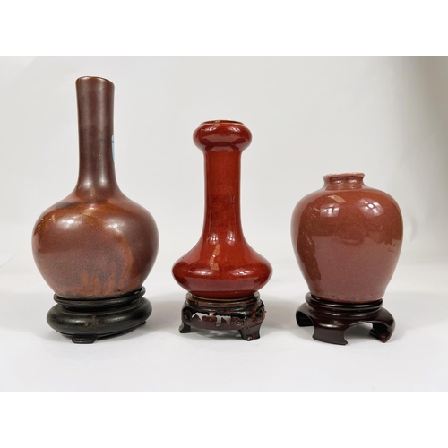 403 - Three Chinese red glazed vases of various shapes and sizes all with hard wood stands, largest, 16cm,... 