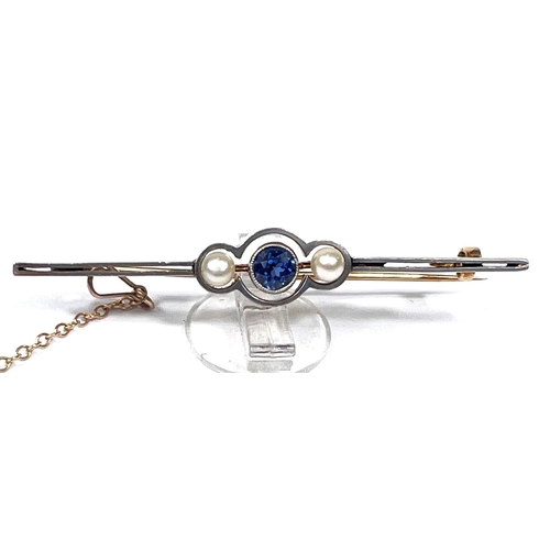 736 - A yellow metal bar brooch set with a central light blue sapphire flanked by two pearls, with safety ... 