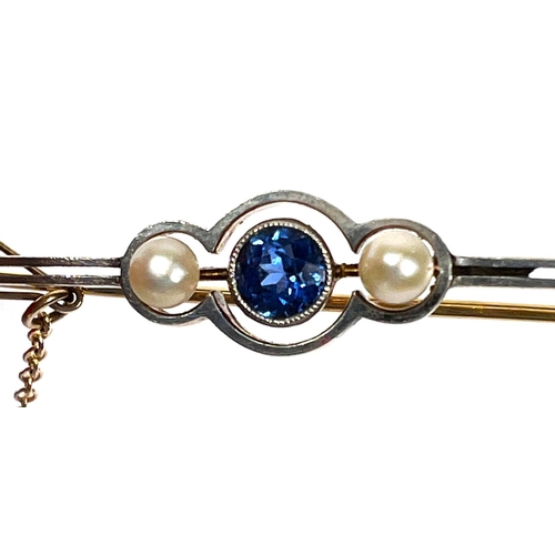 736 - A yellow metal bar brooch set with a central light blue sapphire flanked by two pearls, with safety ... 