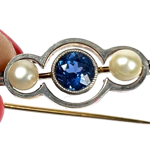 736 - A yellow metal bar brooch set with a central light blue sapphire flanked by two pearls, with safety ... 