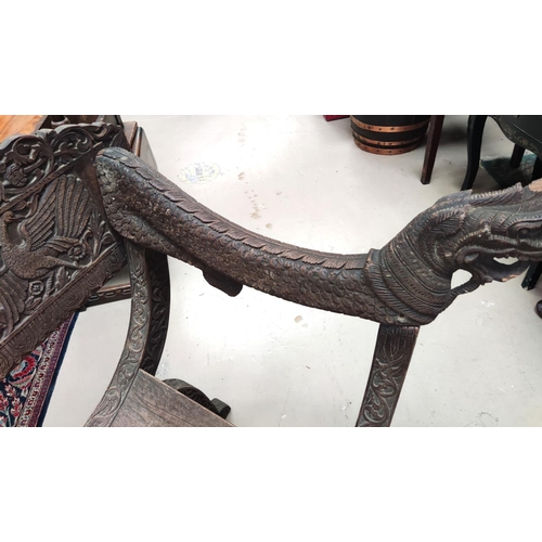 849 - A heavily carved Indonesian arm chair with rounded seat, carved serpent arms, peacock carving to the... 