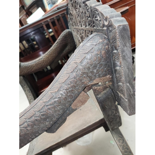 849 - A heavily carved Indonesian arm chair with rounded seat, carved serpent arms, peacock carving to the... 