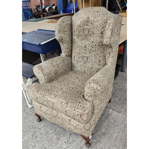 803 - A high wing back armchair upholstered in tapestry style fabric with armorial designs decorating it