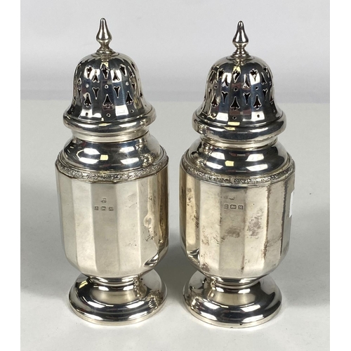 714 - A hallmarked silver pair of sugar dredgers in the Georgian style with pierced domed tops and ribbed ... 