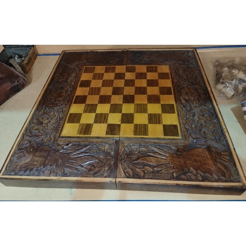 54 - A carved wooden folding chessboard with chess pieces and checkers, parrot carved decorative