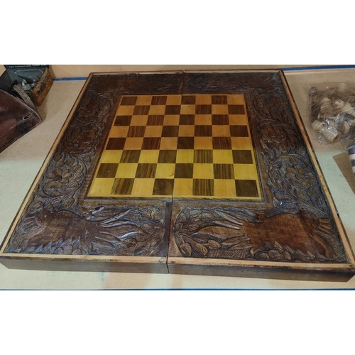 153 - A carved wooden folding chessboard with chess pieces and checkers, parrot carved decorative