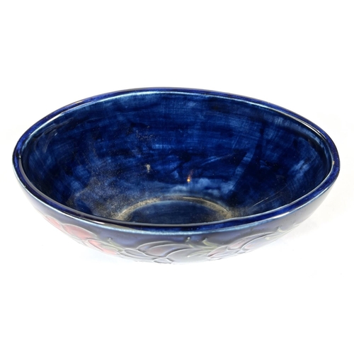 571D - Moorcroft: A Moorcroft boat shaped bowl, dark blue ground, anemone decoration with original pot... 