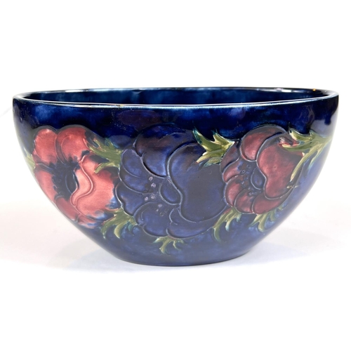 571D - Moorcroft: A Moorcroft boat shaped bowl, dark blue ground, anemone decoration with original pot... 