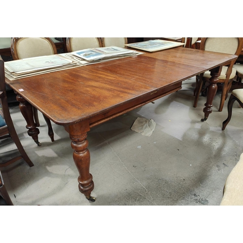 933 - A rounded rectangular Victorian mahogany extending dining table on turned legs and castors, two spar... 