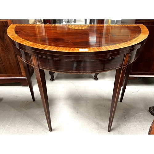 991 - A Sheraton style demi-lune inlaid mahogany card table with wide satinwood crossbanding and shell inl... 