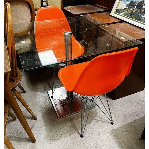 987 - A square glass kitchen table with brushed steel pedestal, two bright orange dining chairs 