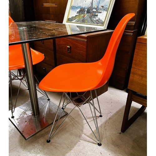 987 - A square glass kitchen table with brushed steel pedestal, two bright orange dining chairs 