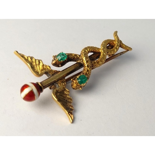 786 - A yellow metal Caduceus brooch set 2 emeralds, enamelled finial, (tests 14ct) base metal pin. 3.74gm... 