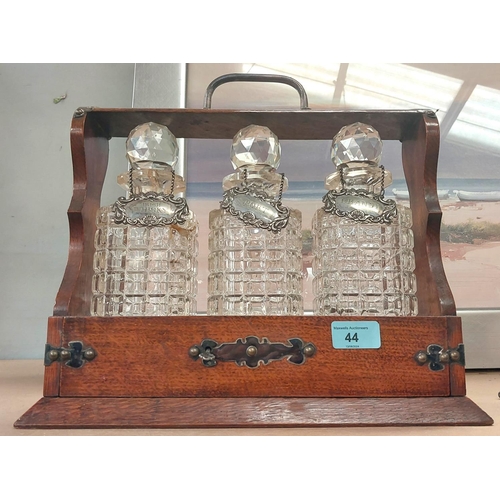 44 - An oak framed Tantalus with silver-plated mounts, fitted 3 hobnail cut decanters (1 a.f.), with meta... 