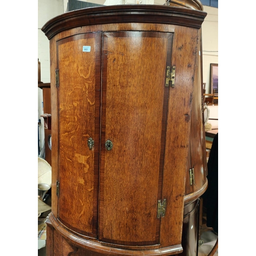 865 - A Georgian oak cross-banded bow front corner cupboard.